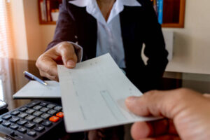 Cropped image of business woman hand giving blank checkbook to another. Paycheck and payroll concept.